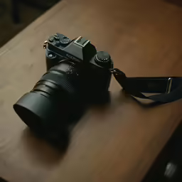 a camera and a strap sitting on a wooden table