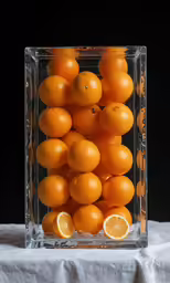 oranges in a square glass vase on top of a white table cloth