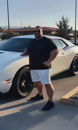 a bald man in shorts leaning on a parked white car
