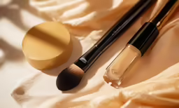 a makeup brush sits next to a powder on a blanket