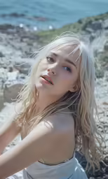 a blonde woman sitting in the sand with her arms on her hips