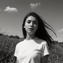 an attractive young woman stands in a field, with long hair flying in the wind