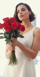 woman in white dress holding bouquet of red roses