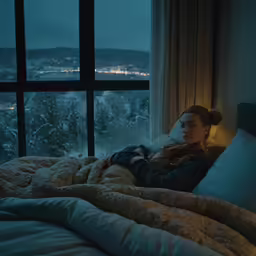 a woman sits on her bed watching out of the window