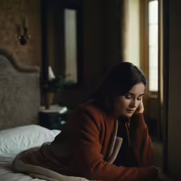 the woman sits on her bed using a laptop