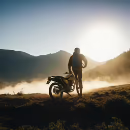 a person standing with a motorcycle in front of a hill