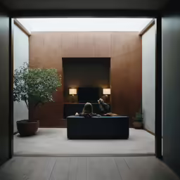 two people sit on the couch with one laying back on his knees