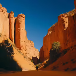 a person walking down a desert trail, towards rocks and a cliff