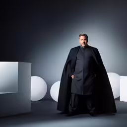 a man wearing a black coat stands next to a white sphere and blocks
