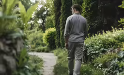 a man in suit walking down a path near many bushes