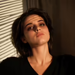 a woman looks up from behind her blinds