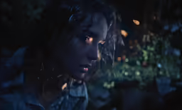 a woman stares into the camera with a light shining down on her face