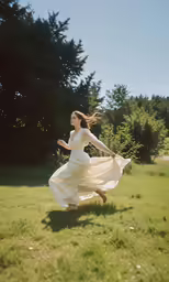 woman in white dress running across field with trees