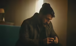 the man is sitting on the couch and checking his cellphone
