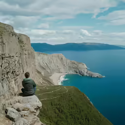 a person is sitting on a cliff overlooking the sea