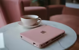 a pink ipod sitting on a marble table near a cup of coffee