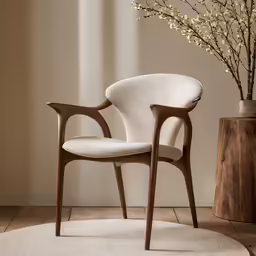 an upholstered armchair sits on a rug with a vase of flowers in the background