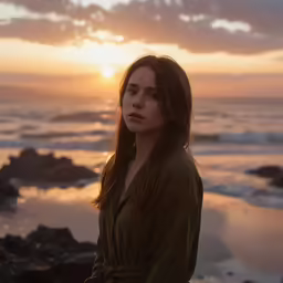 a young woman in an oversize jacket stands on the edge of an ocean
