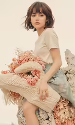 a young woman wearing a dress sitting on top of a pile of flowers