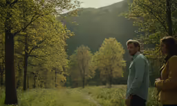 a man and woman look at each other in a wooded area