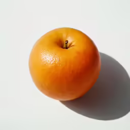 a yellow ripe orange sitting on top of a white surface