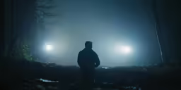 two foggy, lit torches are seen behind a man standing alone