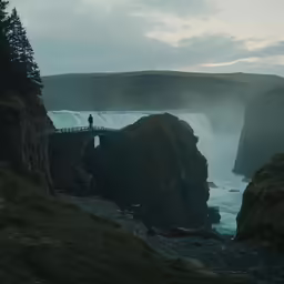 a man stands on a bridge overlooking a waterfall