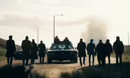 some men and one car standing near a dirt road