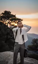 a man wearing suit and tie standing on top of a mountain