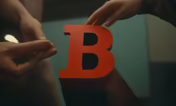 two hands hold the letter b over a red object