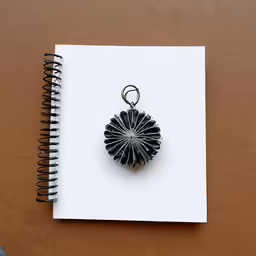 a spiral bound notebook with a silver pendant on the top