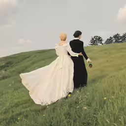 a bride and groom walk across a field with flowers