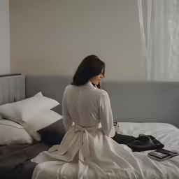 a woman in a white robe sits on the bed