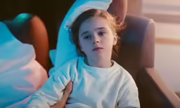the young girl is sitting in bed looking at the camera