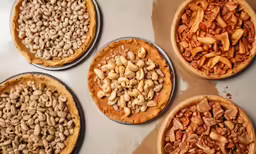 several pizzas in pie pans with nuts on them