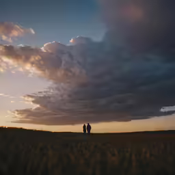 two people walk through an empty field during a dramatic sunset