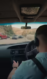 a man wearing head phones and driving a vehicle with a horse on the road behind him