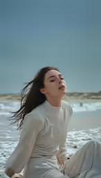 woman sitting on a sandy beach wearing a white gown