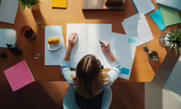 a woman is writing at her desk with lots of office supplies
