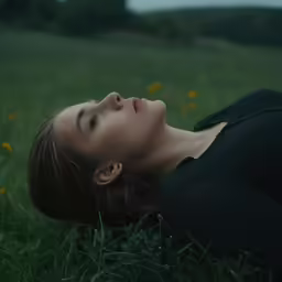 a woman lying in the grass near wild flowers