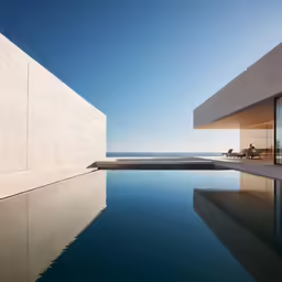 a concrete pool with large windows and a stone terrace near the ocean