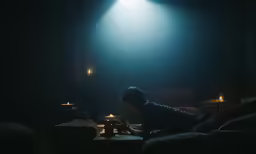 a person sitting in a dark room on a couch next to a table and a lamp
