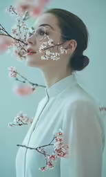 a woman wearing glasses with pink blossom branches in front of her