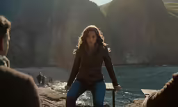 a woman holding a walking stick and walking along a beach with her back turned to the camera