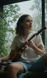 a woman sitting on a window sill playing a guitar