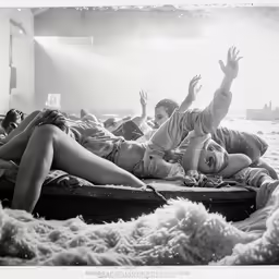 two girls and one boy laying in a bed, the man waving from behind them