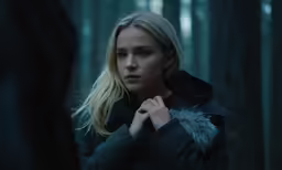 a woman is wearing a jacket and standing in the woods