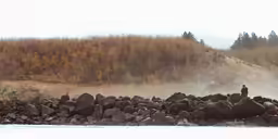a man on a boat with a water gun standing next to rocks