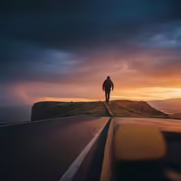 the lone person stands on the edge of the cliff at sunset