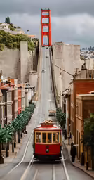 the red trolley car is on the tracks beside the bridge